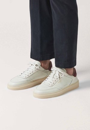 Baskets en cuir de couleur blanc cassé avec un accent de talon marron, dotées d'une semelle plate, d'un embout rond et de détails perforés sur le dessus.