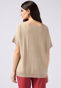 Top in maglia beige a maniche corte con scollatura ampia e dettagli a costine, caratterizzato da una leggera lucentezza e cuciture verticali sul retro.
