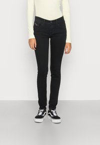 Jeans negros ajustados con una cintura alta, bolsillos frontales y detalles de costura sutiles, combinados con zapatillas blanca y negras.