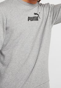Szara bluza z miękkiej tkaniny, z czarnym logo Puma na piersi i prążkowanym okrągłym dekoltem.