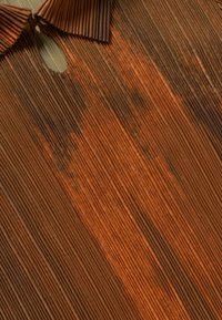 Bruin geplooid textiel met verticale lijnen, voorzien van een ronde halslijn en een uitsnijdetail. De textuur lijkt scherp met verschillende tinten.