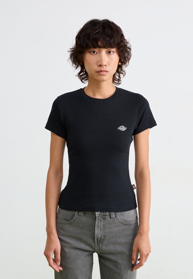 Sort tætsiddende t-shirt med korte ærmer, ribbet tekstur, rund halsudskæring og lille logo detalje på brystet. Matchet med grå jeans.