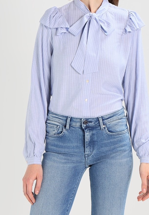 Hellblau gestreifte Bluse mit Rüschenschultern und einer Krawattenkragen, kombiniert mit hellblauen Jeans, die einen lässigen, maßgeschneiderten Look zeigen.