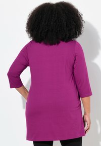 Fuchsia lange Tunika mit ¾-Ärmeln, aus weichem Material, mit abgerundetem Saum und lockerer Passform; die Rückansicht zeigt eine glatte Textur und Silhouette.
