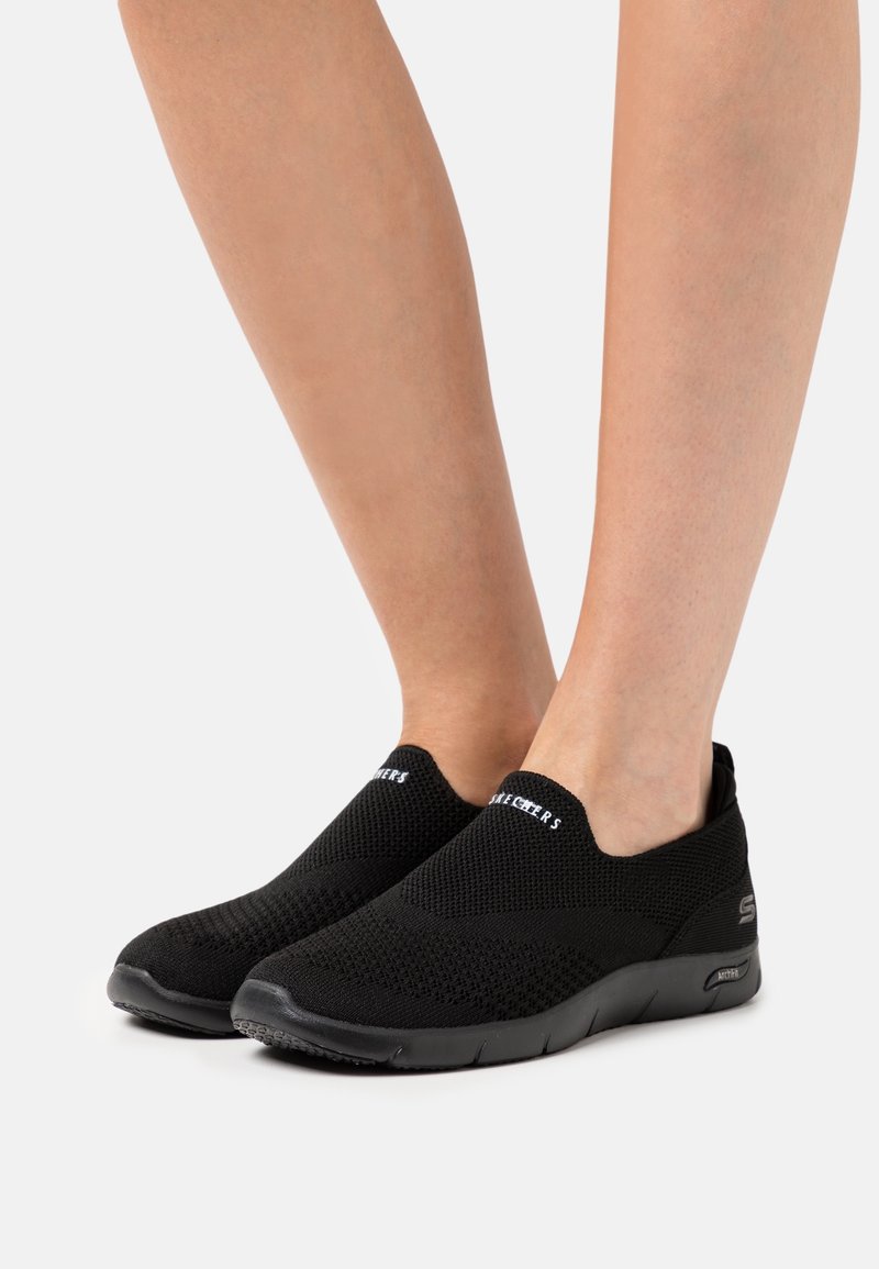 Scarpe slip-on nere con tomaia in rete traspirante, design testurizzato e suola flessibile. Presentano il logo sulla parte anteriore superiore e una costruzione leggera.