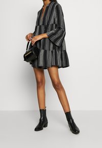 Robe à volants rayée noir et blanc avec des manches longues, décolleté en V profond et tissu texturé ; assortie à un sac à main noir et des bottines.