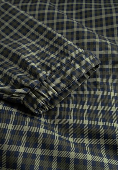 Primo piano di un tessuto a quadri verde e blu navy con dettaglio di polsino elasticizzato, che mostra la trama e il motivo sul materiale piegato.