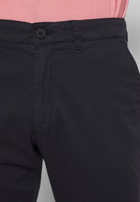 Czarne spodnie z tkaniny z zapięciem na guzik, zamkiem błyskawicznym i kieszeniami po bokach, o gładkiej fakturze i dopasowanym kroju.