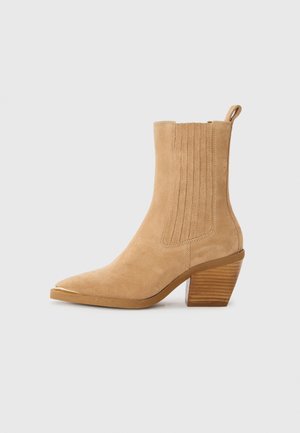 Botine din suede bej cu vârful ascuțit și detalii cu design ribat, având toc bloc și o mică bandă de prindere în spate.