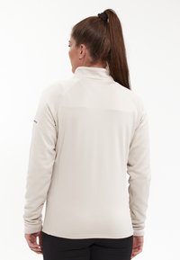 Ljus beige fleecejacka med hög krage, långa ärmar och en mjuk textur, med en sömdesign och en figursydd siluett.