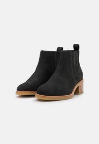 Bottines en suède noir avec un bout arrondi, des côtés élastiques et un talon empilé texturé marron. Présente des languettes à l'arrière pour un enfilage facile.