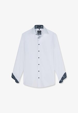 Chemise blanche à manches longues avec boutons noirs et motifs floraux foncés à l’intérieur du col et des poignets, présentée avec les manches partiellement retroussées.