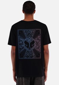 Black t-shirt featuring a colorful graphic on the back with abstract designs and a central emblem, set against a dark background.