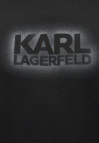 Μαύρο ύφασμα με το όνομα της μάρκας «KARL LAGERFELD» τυπωμένο στο κέντρο με μεγάλα, έντονα γράμματα σε λευκή απόχρωση με διαβάθμιση.