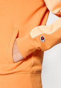 Πορτοκαλί φούτερ με μπροστινή τσέπη και ριμπ μανσέτες. Διαθέτει ανοιχτό πορτ οκαλί λεπτομέρειες στα μανίκια και λογότυπο στο μανίκι. Μαλακή υφή.