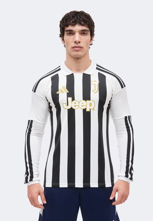 Mężczyzna w czarno-białej, paskowanej koszulce piłkarskiej Juventusu z złotym logo Jeep i paskami Adidas na rękawach, zwrócony przodem.