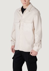 Beige overhemd met knopen, twee borstzakken, lange mouwen en een relaxed fit. Gemaakt van zacht materiaal; heeft een klassieke kraag en manchetten.