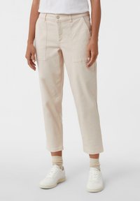 Jasno beżowe spodnie typu crop wykonane z bawełny, z dwoma przednimi kieszeniami, zapięciem na guzik oraz prostym krojem nogawek, w połączeniu z białymi trampkami.