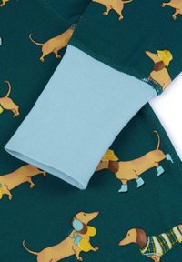 Tessuto di cotone stampato con bassotti in teal, con polsini azzurri chiari a coste e illustrazioni di cani giocosi in vari vestiti.