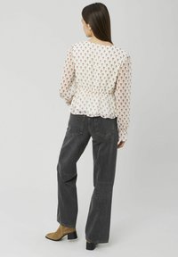 Blouse à motif floral avec manches longues, taille cintrée et ourlet à volants, associée à un jean gris foncé taille haute et des bottines marron.