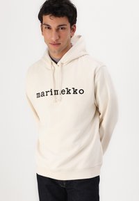 Krém színű kapucnis pulóver fekete "marimekko" felirattal, stávolt, puha, texturált anyagból. Sötét farmerral párosítva.