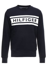 Námořnická mikina se širokým výstřihem, s bílým horizontálním pruhem a textem "HILFIGER" v tučné černé barvě. Měkký materiál a žebrované manžety.