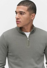 Sweter z pulowerem w jasnym oliwkowym kolorze, z zamkiem błyskawicznym w stójce, prążkowaną teksturą i dopasowanym fasonem. Minimalistyczny styl bez wzorów.