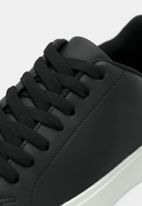 Must Black synthetic leather sneaker, mille mustade lindi, siledal ülemisel pinnal, diskreetne õmblus ja valge kummist tallaga.