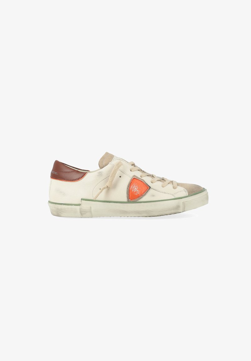 Zapatilla baja blanca y beige con una lengüeta en el talón marrón, logo en forma de escudo naranja en el costado, y suela y cordones ligeramente usados.