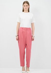 Witte t-shirt met korte mouwen, gecombineerd met hooggeprijsde roze broeken met plooien en een knoopsluiting. Model draagt beige hakken.