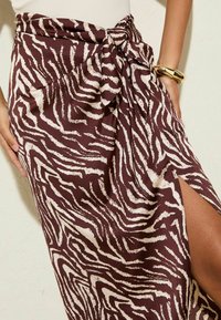 Bruine en crèmekleurige zebra print wikkelrok met een strik taille detail en een zijsplit. Gemaakt van een gladde stof met een zachte textuur.