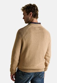 Bež plekk-sviiter, millel on soonikkoes varrukad ja äär, ümar kaelus ning kontrastne tekstuuriga seljaosa. Kombineeritud siniste teksadega.