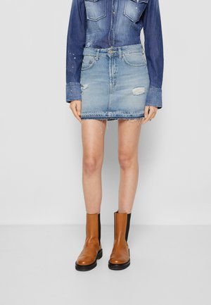 Falda de denim en azul claro con áreas desgastadas y dobladillo deshilachado. Combinada con botas de tobillo marrones que tienen un panel lateral elástico negro.