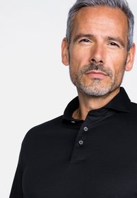 Schwarzes Polohemd mit Kragen, ausgestattet mit drei Knopfverschlüssen. Der Stoff wirkt glatt mit einem leichten Glanz. Sichtbare Qualitätsnähte.