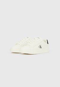 Weiße Sneaker aus glattem Material mit schwarzem Fersenakzent und besticktem Logo an der Seite, flachen Schnürsenkeln und abgerundeter Spitze.