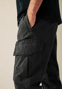 Black cargo pants made of lightweight fabric, featuring large side pockets, a relaxed fit, and a waistband that sits comfortably.