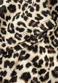 Tkanina z leopardskim vzorcem, ki prikazuje mešanico svetlo bež, črnih in rjavih madežev na mehkem tekstilu. Ima raven šiv blizu roba.