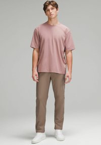 Lyhythihainen, pyöreäkauluksinen t-paita pölyruusuisena, yhdistettynä vaaleanruskeisiin, kapeisiin housuihin ja valkoisiin lenkkikengiin, joissa on sileä pinta.