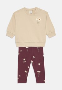 Beiger Pullover mit floraler Stickerei und Druckknöpfen, kombiniert mit burgunderfarbenen Leggings mit einem weißen Gänseblümchenmuster. Weiches Baumwollmaterial.