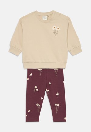 Beige sweatshirt met bloemenborduursel en drukknoopsluiting, gecombineerd met bordeaux leggings met een witte madeliefjesprint. Zachte katoenen stof.