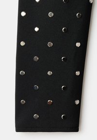 Černá tkanina s kulatými kovovými hrotky uspořádanými v pravidelném vzoru. Hrotky se liší barvou, zahrnují stříbrnou, černou a tmavě modrou.