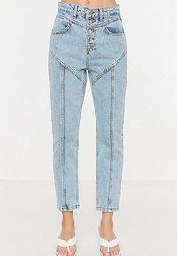 Světle modré džíny s vysokým pasem a knoflíkovým zapínáním, s jedinečnými předními švy a dvěma bočními kapsami. Materiál je denim s hladkou texturou.