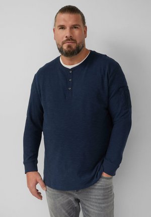 Marineblaues Langarm-Henley-Shirt mit Rundhalsausschnitt, Knopfleiste mit drei Knöpfen und seitlicher Taschenoptik. Der Stoff hat eine strukturierte Oberfläche.