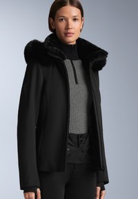 Crna softshell jakna s krznom od umjetne kože, s patentnim zatvaračem sprijeda, visokim ovratnikom i teksturiranim pletenim slojem ispod. Glatka tkanina s prilagođenim siluetom.