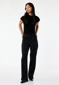 Top negro de manga corta combinado con pantalones oscuros texturizados que presentan sutiles líneas verticales brillantes. El calzado es negro y de punta.