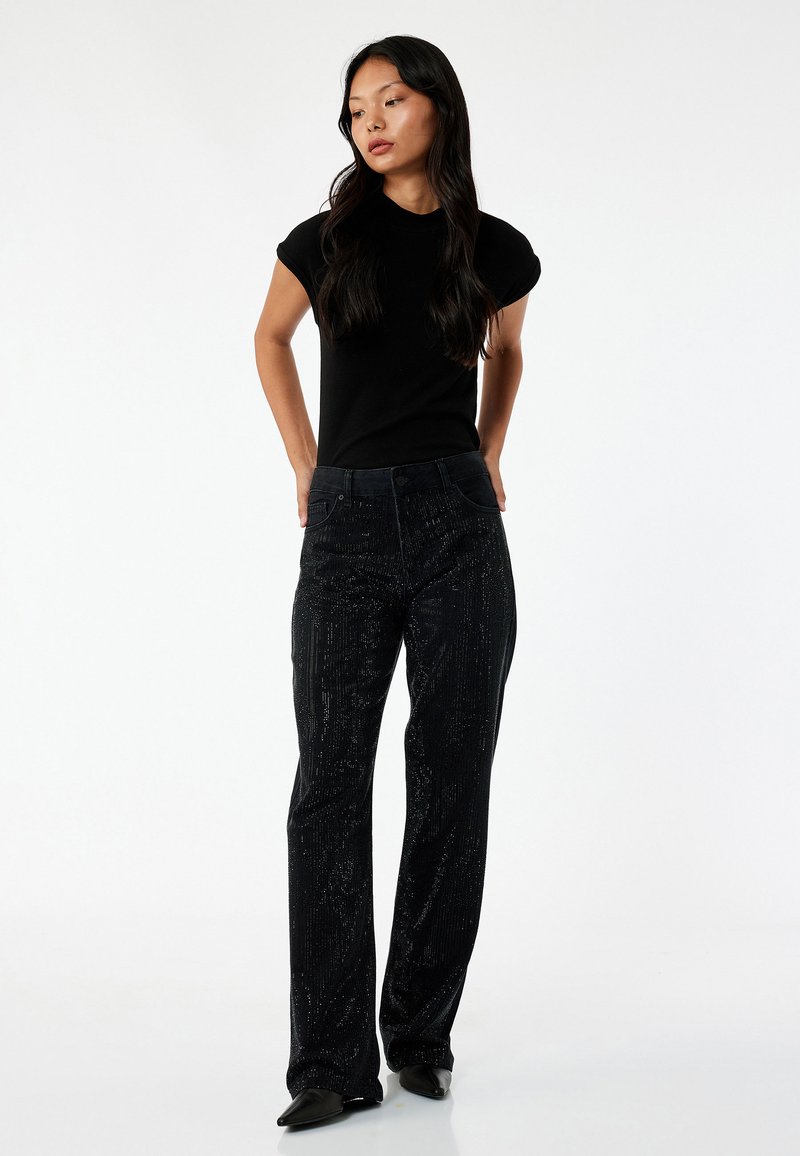 Top negro de manga corta combinado con pantalones oscuros texturizados que presentan sutiles líneas verticales brillantes. El calzado es negro y de punta.