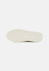 Weiße Sneaker-Sohle mit einem strukturierten Fischgrätenmuster und einer zentralen Logo-Platte, die "AX" und "Armani Exchange" zeigt.