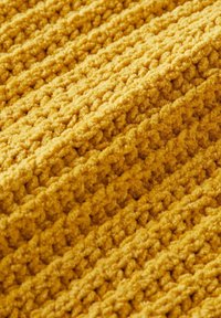 Tela amarilla texturizada con una superficie suave y peluda. Surcos verticales crean un patrón a rayas, enfatizando la gruesa y esponjosa textura del material.