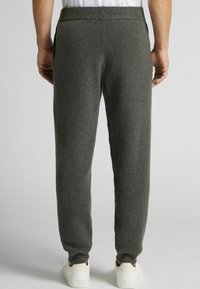 Šedé pletené tepláky s texturovaným povrchem, elastickým páskem a zúženými manžetami, nošeny s bílými teniskami a šedým pozadím.