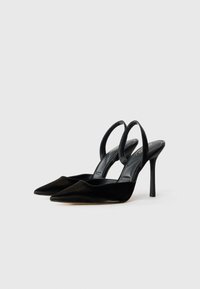 Mustat samettiset slingback-korkokengät, joissa on terävät varpaat ja kapeat stiletto-korkokengät. Sisäpuolella on sileä musta vuori ja hillitty brändäys.